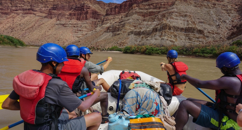 A group of people wearing safety gear navigate a raft.